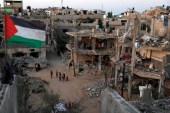 A Palestinian flag flies next to the ruins of houses destroyed by Israeli air strikes during the recent Israeli assault on Gaza on May 25, 2021. [Reuters/Mohammed Salem]