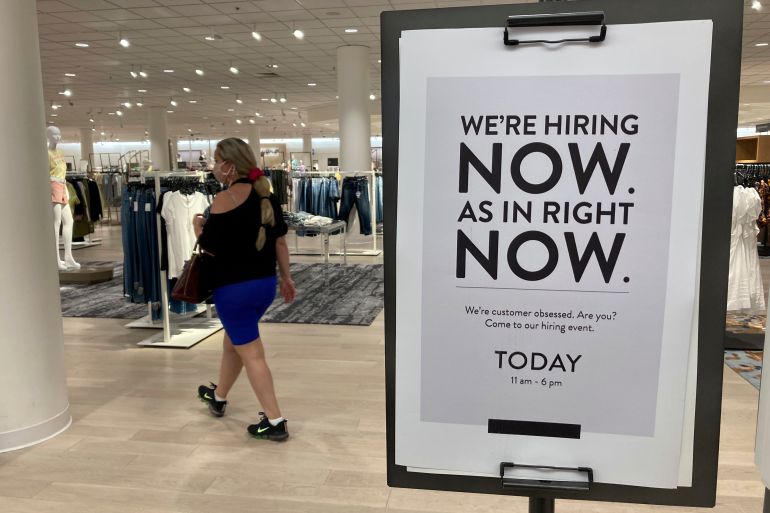 A customer walks behind a sign at a Nordstrom store seeking employees, in Coral Gables, Florida, US