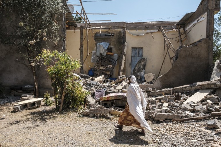 A woman walks in front of a damaged house in Tigray [File: Eduardo Soteras/AFP]