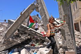 Palestinian children wave Palestinian flags as they play in the rubble of buildings destroyed by an Israeli bombardment, in Khan Younis, in the southern Gaza Strip on June 19, 2021 [Said Khatib/ AFP]