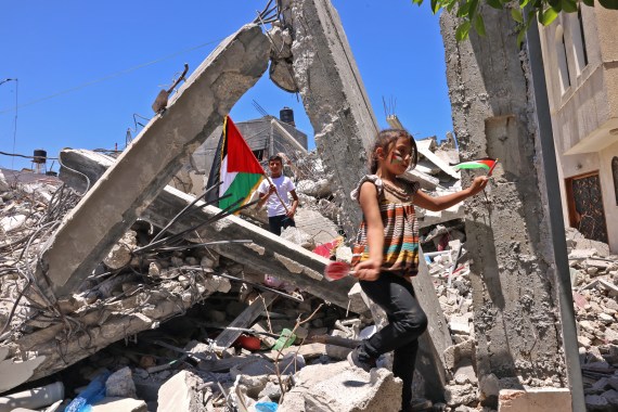 Palestinian children wave Palestinian national flags as they play among the rubble of buildings