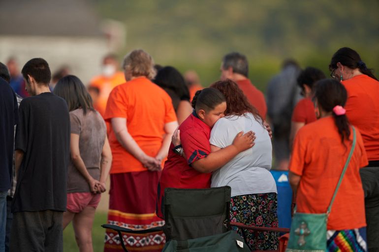 people hug in a field where unmarked graves were discovered