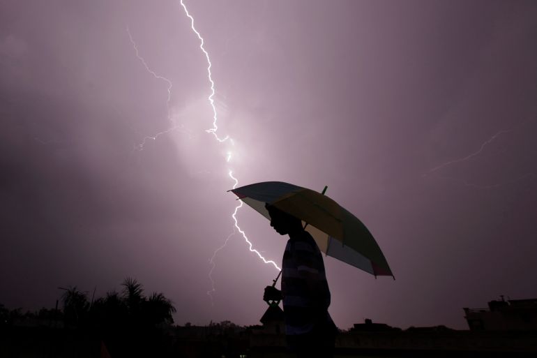A pedestrian walks with an umbrella as lightning strikes during an evening thunderstorm