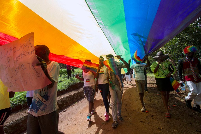 People walk under a giant rainbow flag as they take part in the Gay Pride parade in Entebbe on August 8, 2015. Ugandan activists gather [Isaac Kasamani/AFP]