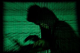 Photo illustration of a hooded man in front of a computer