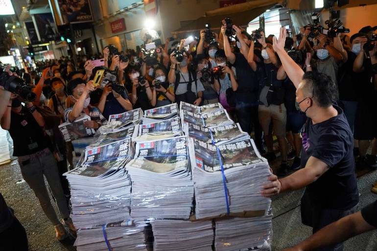 Bir adam, Apple Daily'nin son baskısı ile dolu bir paleti gazete bayisine getirirken el hareketi yapıyor.