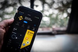 Hand showing the Binance Exchange application for download in the Apple Inc. App Store on a smartphone