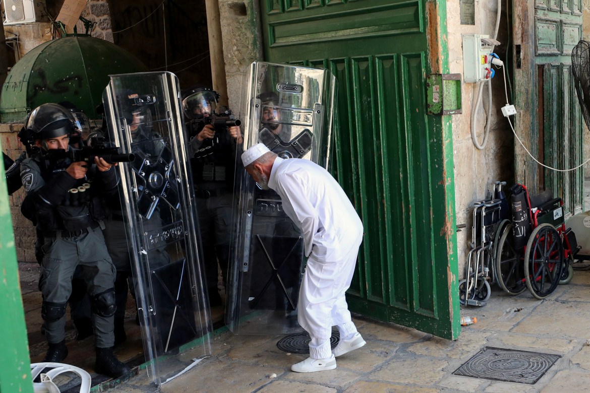 A Palestinian man tries to leave Al-Aqsa Mosque as Israeli security force members aim their weapons at Palestinians in the compound. [Ammar Awad/Reuters]