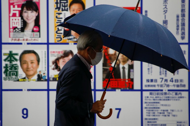 A voter wearing a protective face mask walks past a board displaying posters of candidates for the Tokyo Metropolitan Assembly election near a polling station, amid the COVID-19 outbreak, in Tokyo, Japan, July 4, 2021 [Issei Kato/ Reuters]