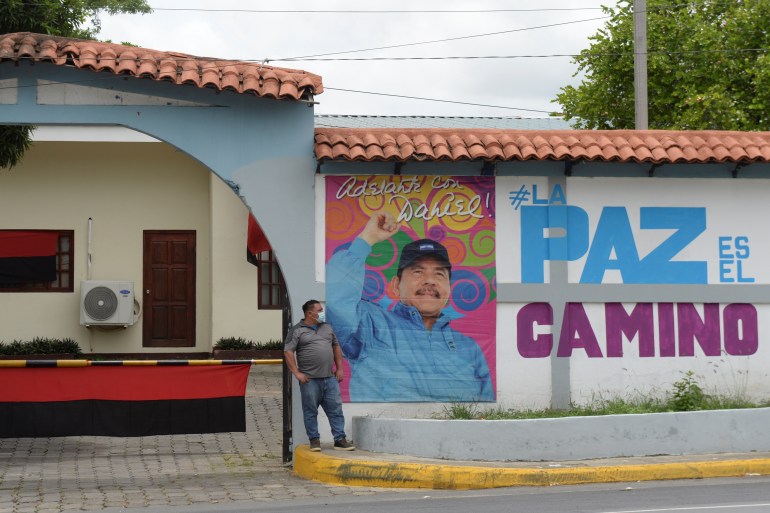 A man stands next to a photo of Nicaraguan President Daniel Ortega on a wall promoting his candidacy for the upcoming November 7 election, in Managua on June 30 [Stringer/Reuters]