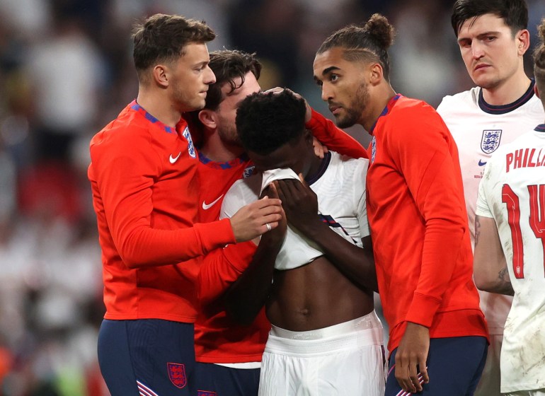 England's Bukayo Saka looks dejected after losing the penalty shootout as teammates console him.