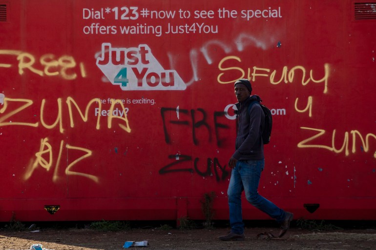 A man walks past graffiti reading "free Zuma" and "we want Zuma" outside a shopping mall in Vosloorus, east of Johannesburg, South Africa, on Wednesday, July 14, 2021 [AP Photo/Themba Hadebe]