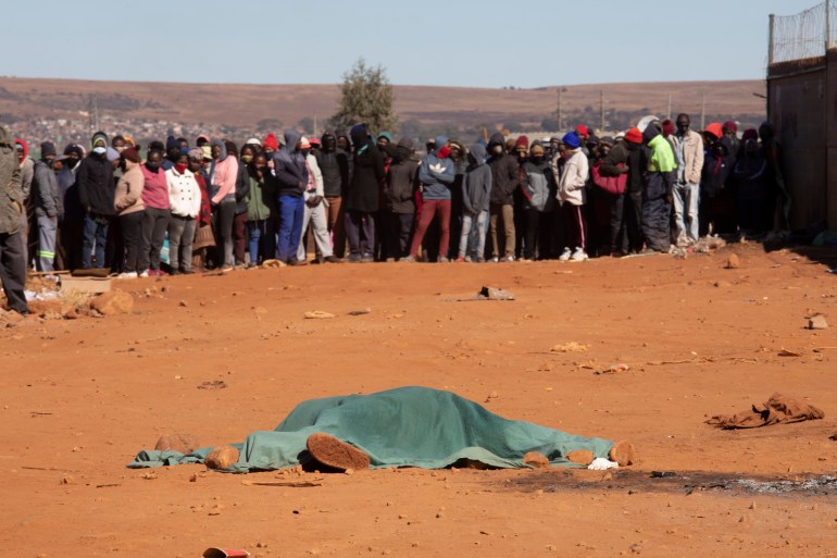 Crowds gather near a body of a looter in Johannesburg after some of the worst unrest in South Africa since the end of apartheid [Kim Ludbrook/EPA]