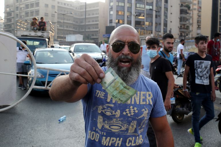 A man gestures with a currency note as Lebanese protesters block the roads with garbage bins and burning tires during protests after Lebanese Prime Minister-Designate Saad Hariri abandoned his effort to form a new government, in Beirut, Lebanon, 15 July 2021.