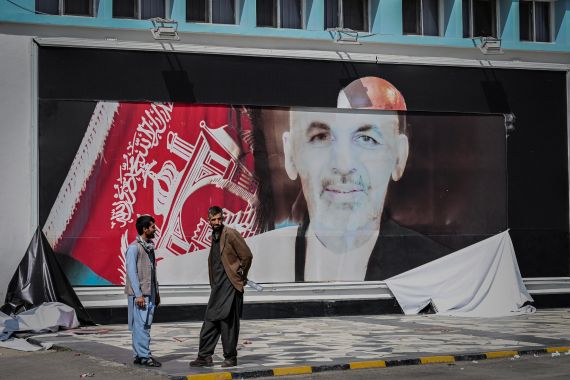 Afghan men stand next to a torn poster of former Afghan President Ashraf Ghani