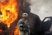 An American soldier stands near a burning M-ATV armoured vehicle after it struck an improvised explosive device in the Arghandab Valley north of Kandahar on July 23, 2010 [File: Reuters/Bob Strong]