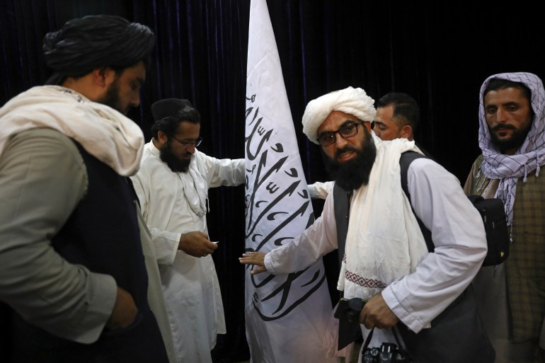 Taliban officials arrange a Taliban flag, before a press conference by Taliban spokesman Zabihullah Mujahid, at the Government Media Information Center, in Kabul, Afghanistan, Tuesday, August 17, 2021 [Rahmat Gul/AP Photo]