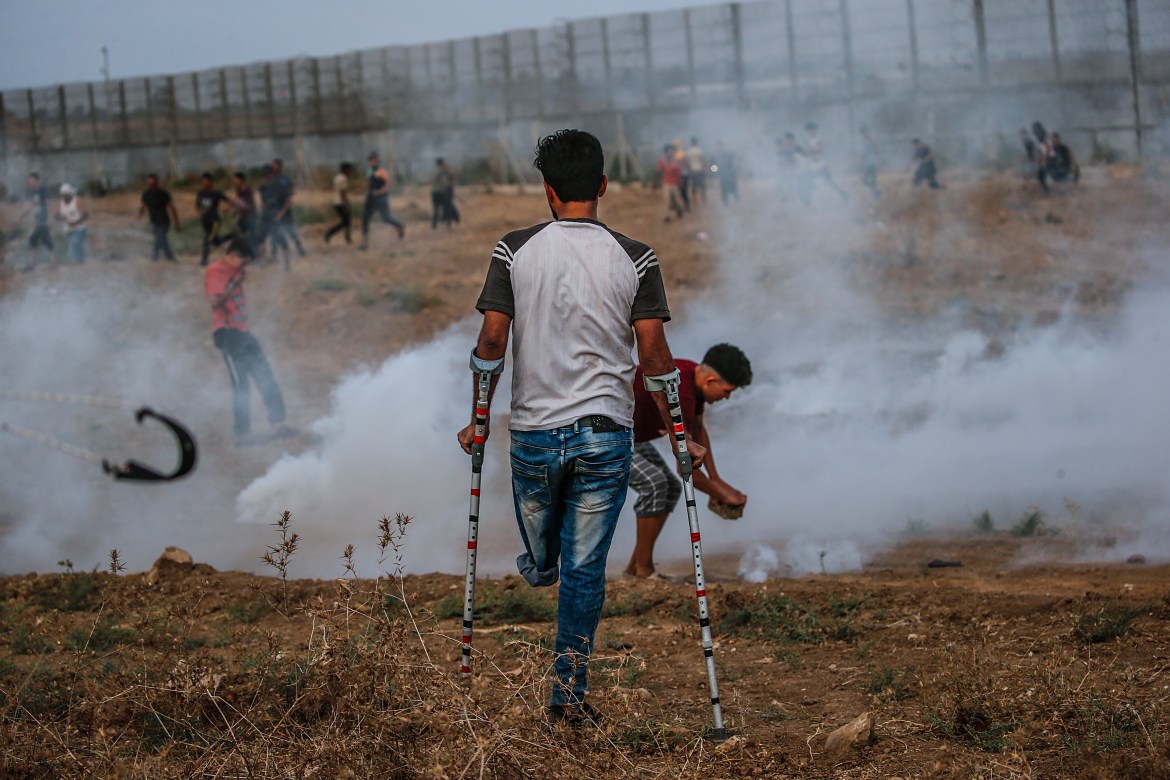 Palestinian protesters take cover from Israeli tear gas during the clashes near the fence. [Mohammed Saber/EPA]