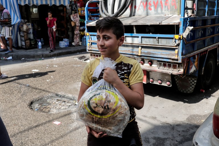 A young boy leaves a bakery with a bag of bread.