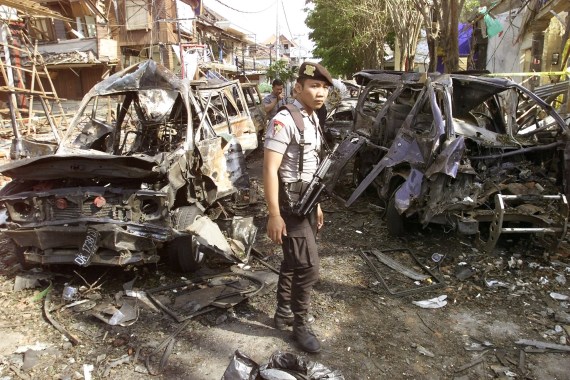 An Indonesian police officer in beige uniform stands amid the wreckage of blackened cars and ruined buildings after the 2002 Bali bombings