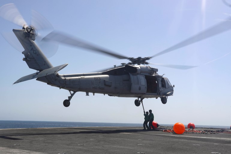 This file photo shows US Navy sailors connecting pogo sticks, used to transport cargo, to an MH-60S helicopter in June 2019 [File: Matt Herbst/US Navy/Handout via Reuters]