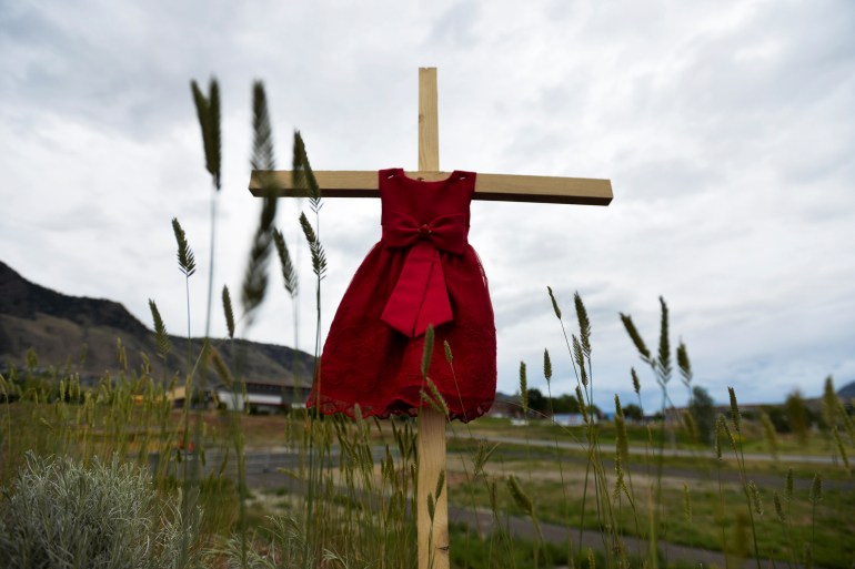 a child's red dress hangs on a stake near grounds where unmarked graves were found