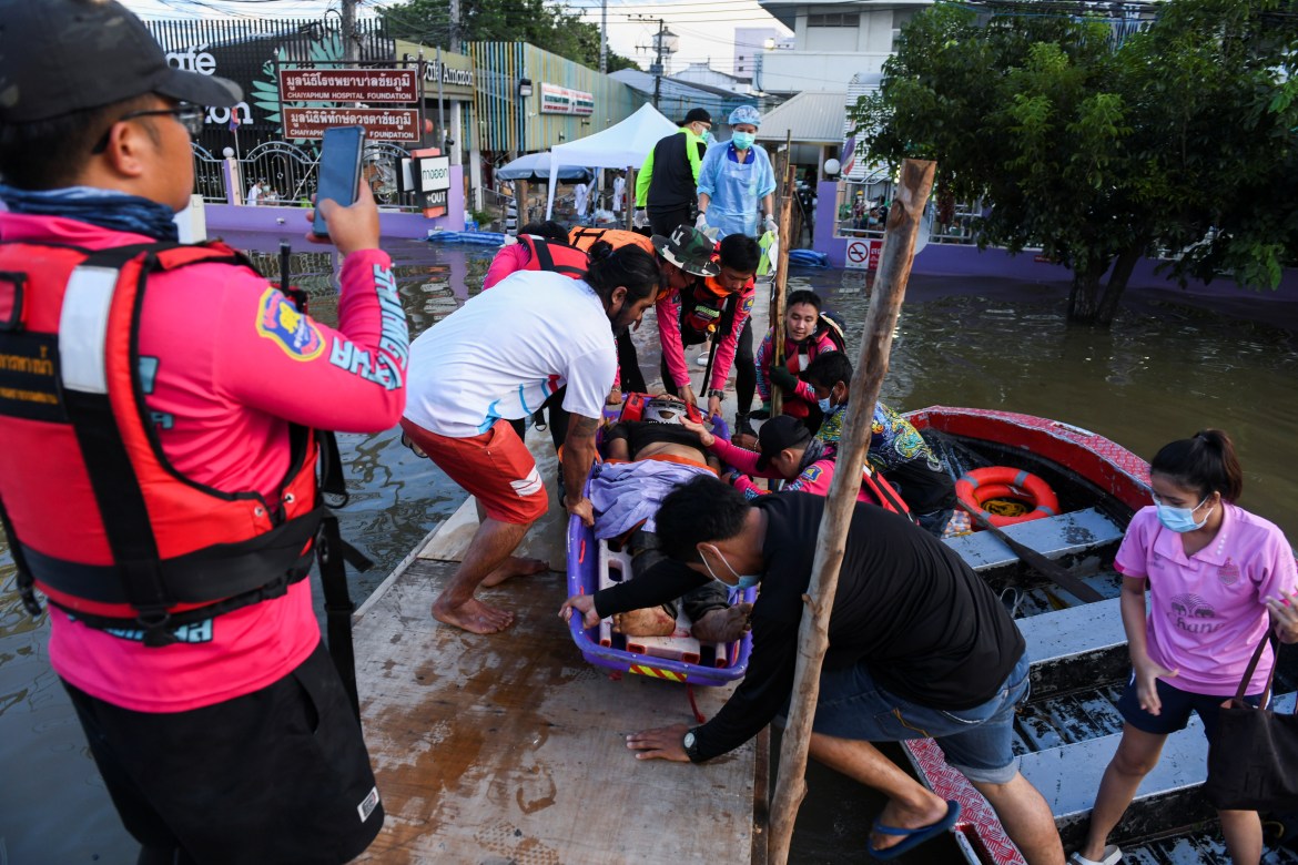 Rescue workers remove a man from a boat on a temporary bridge along a flooded street in front of a local hospital in Chaiyaphum. [Panumas Sanguanwong/Reuters]