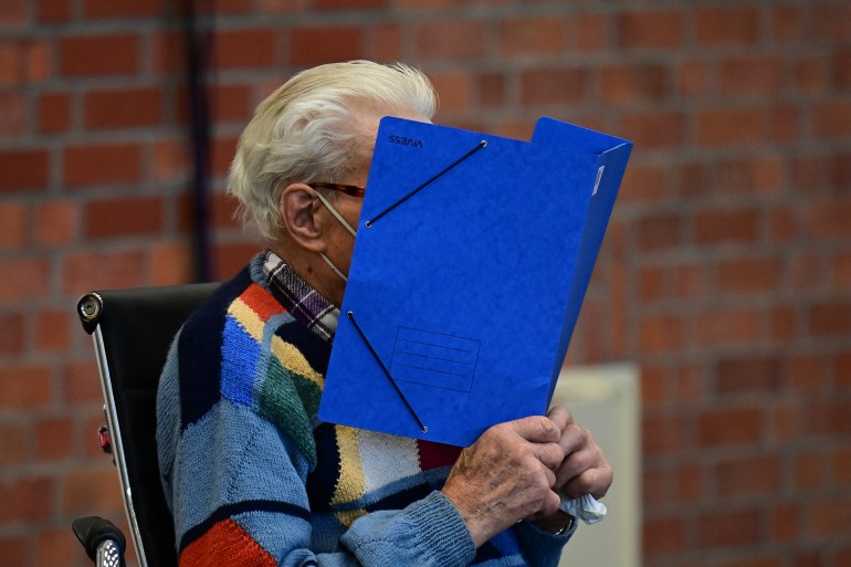 Defendant Josef Schuetz hides his face behind a folder
