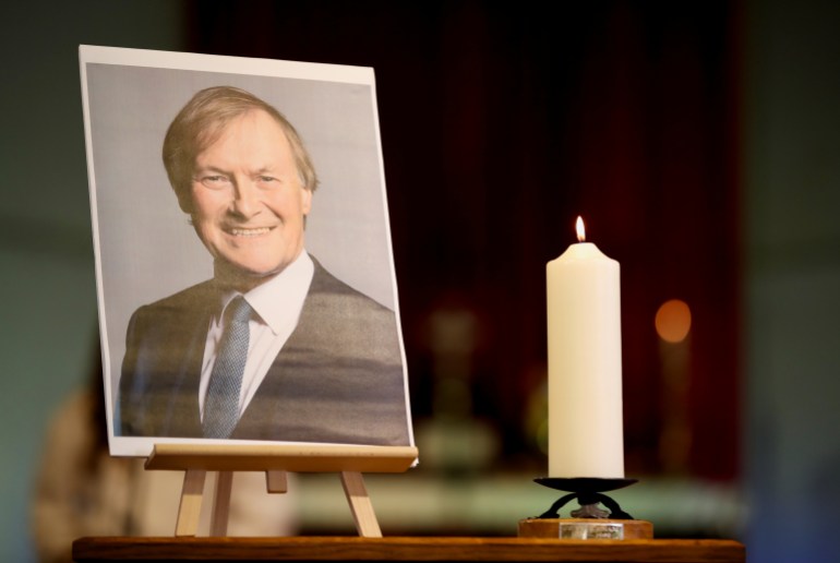 A candle and a portrait of British MP David Amess