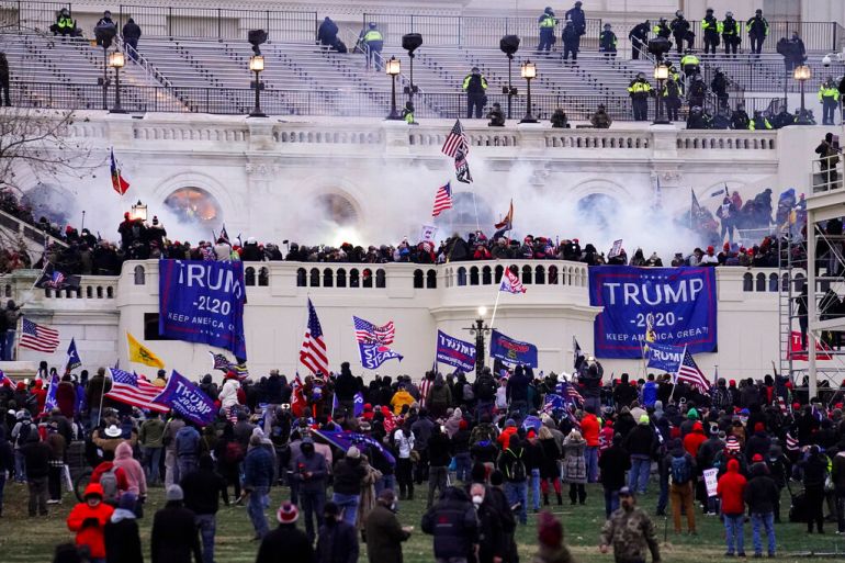Hundreds of supporters of then president Donald Trump, carrying US and Trump 2020 flags, are seen as they storm the Capitol Hill with white smoke in the back ground.