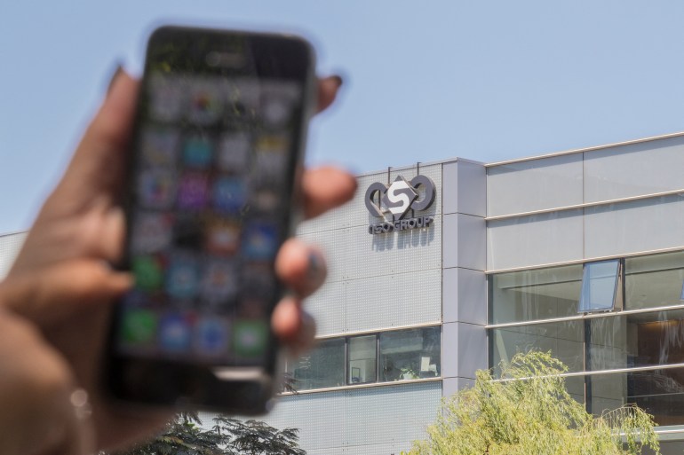 An iPhone is held up in front of a building with the NSO group logo on it