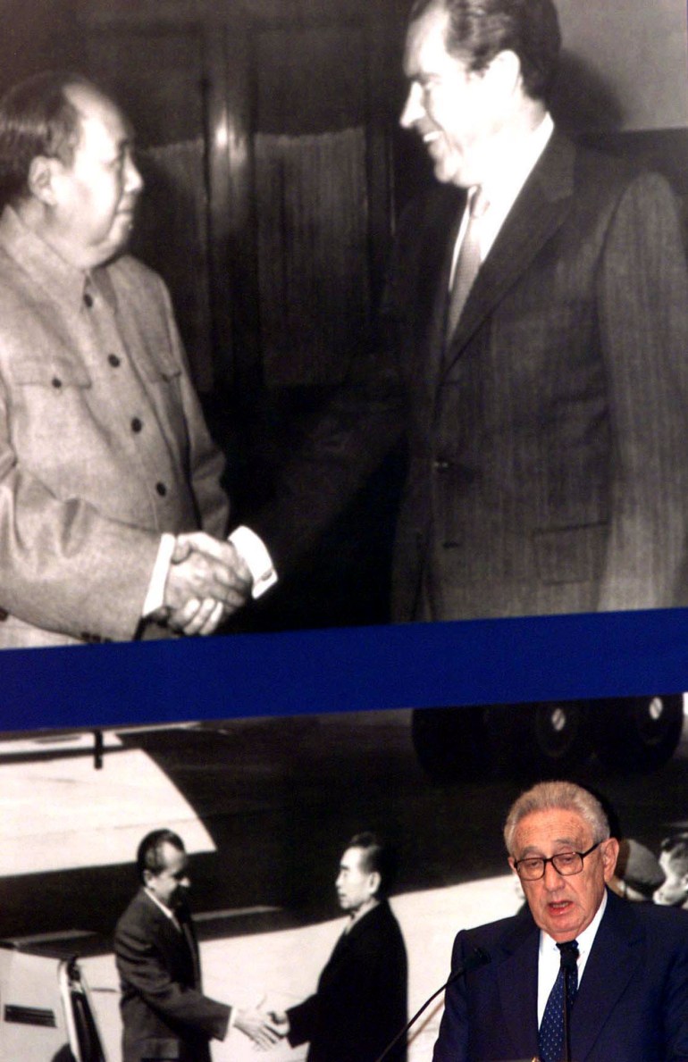 Henry Kissinger speaks in front of an enlarged image of Mao Zedong greeting Richard Nixon.