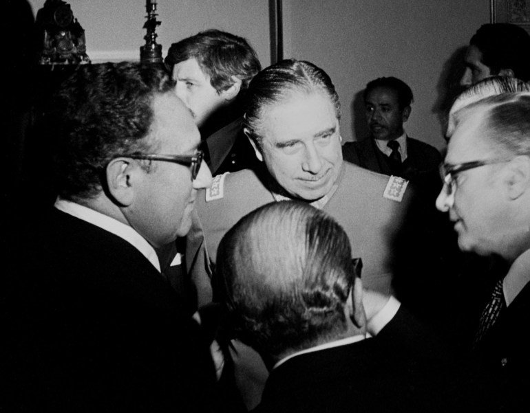 Henry Kissinger ve Augusto Pinochet küçük bir erkek çemberinin içinde duruyorlar.