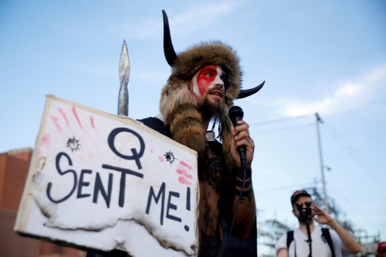 Jacob Chansley, known as the QAnon Shaman, holds up a sign that reads, 