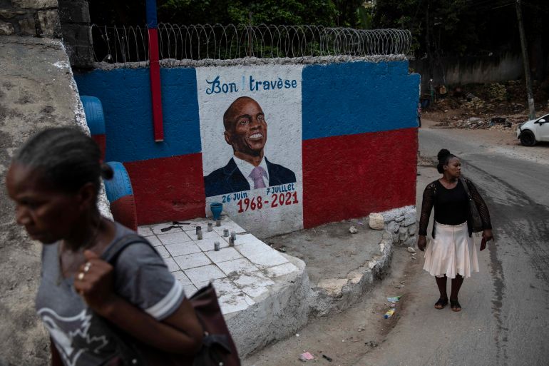 Women walk next to a mural depicting slain Haitian President Jovenel Moise
