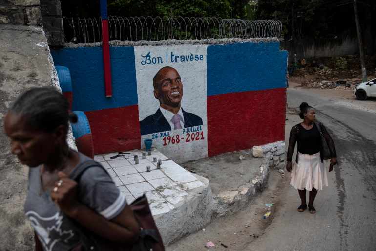 Women walk past a mural depicting Haitian president Jovenel Moise killed