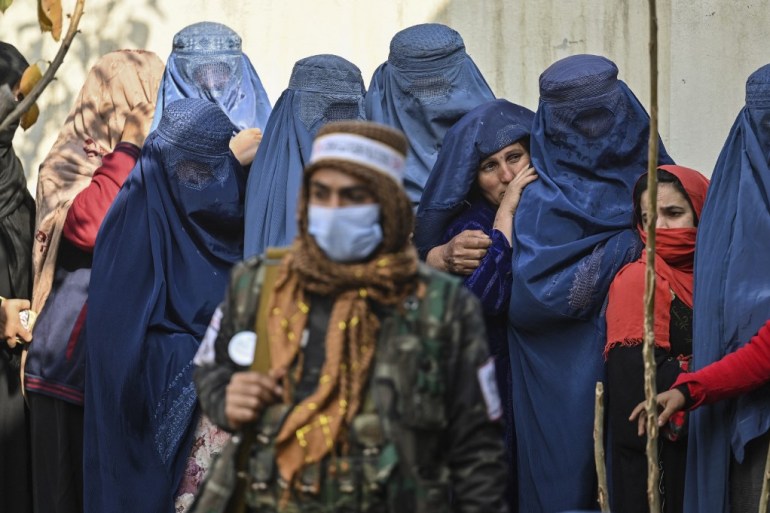 A Taliban fighter stands guard as women wait in a queue during a World Food Programme cash distribution in Kabul on November 29, 2021.