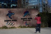 A woman takes a photo of the logos of Beijing 2022 Winter Olympics and Paralympic Winter Games in Shougang Park, one of the sites for the Olympics, in Beijing [File: Noel Celis/AFP]