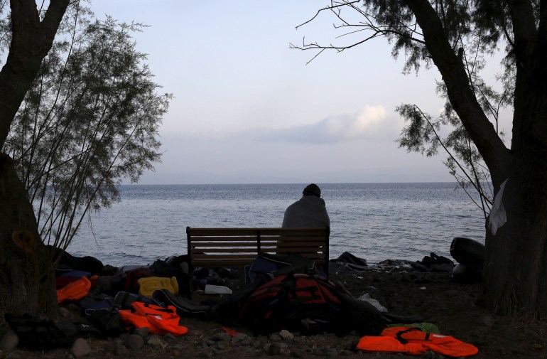 A refugee rests on a bench next to abandoned life vests after arriving at a beach on the Greek island of Lesbos