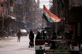 A national flag depicting a picture of Syria's President Bashar al-Assad flutters at a checkpoint in Douma