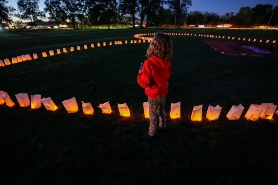 A child stands next to candles representing unmarked Indigenous child graves