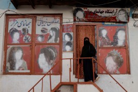 An Afghan woman stands outside a beauty parlor where the pictures of women's faces have been blanked out