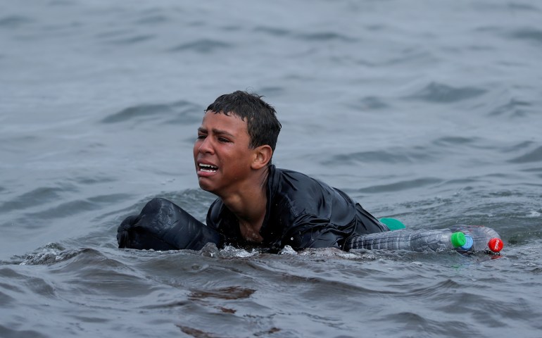 A teen cries as he swims using bottles as floaters near the fence between the Spanish-Moroccan border in Ceuta
