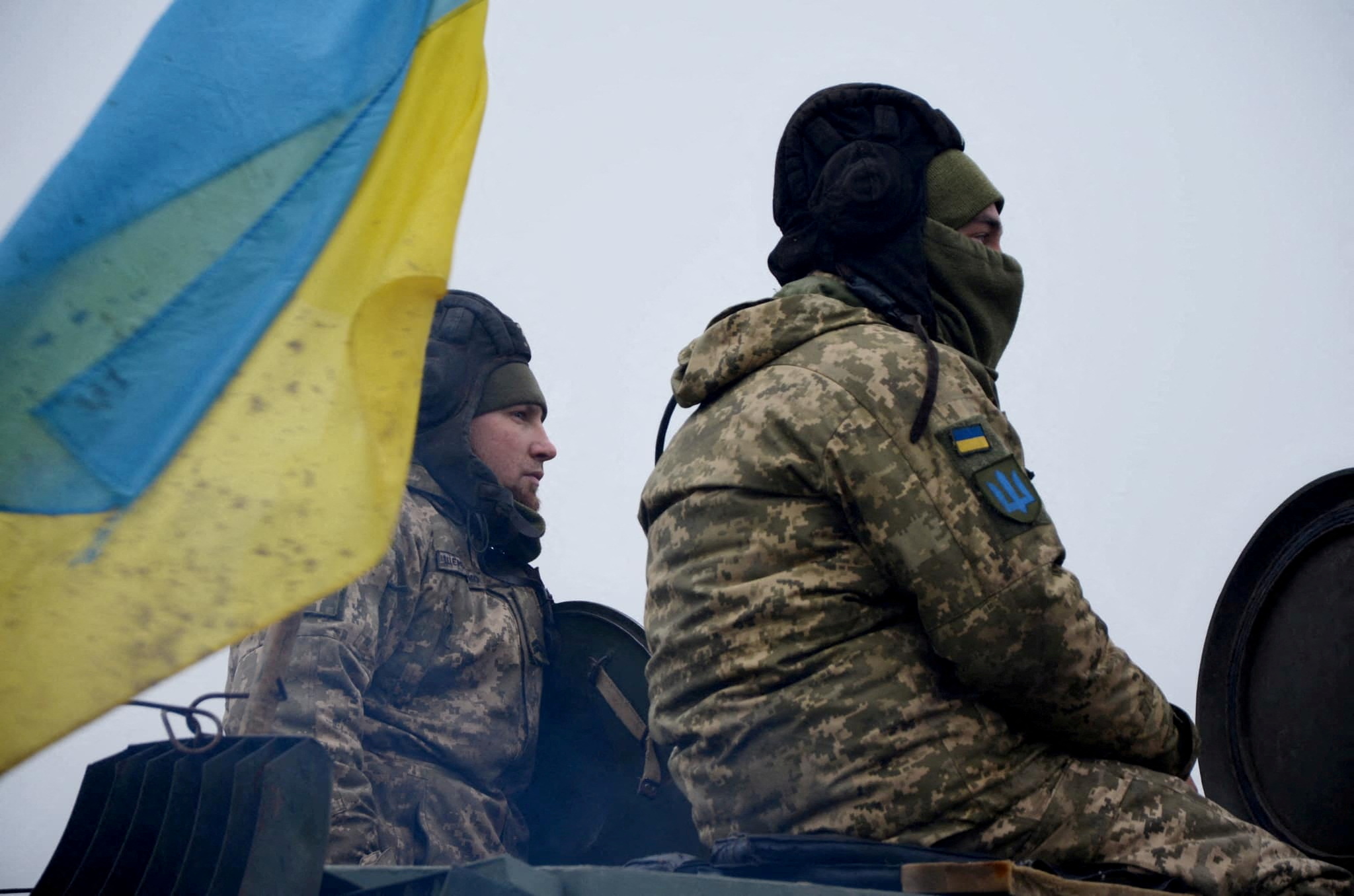 Dois soldados sentam-se perto de uma bandeira ucraniana.