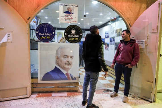 Two men stand next to a picture of Libya's eastern commander and presidential candidate Khalifa Haftar, pasted on the glass facade of a cafe in Benghazi, Libya