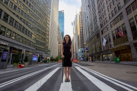 Rebecca with her cane poses for a portrait on a crosswalk in the middle of an empty street in Manhattan.