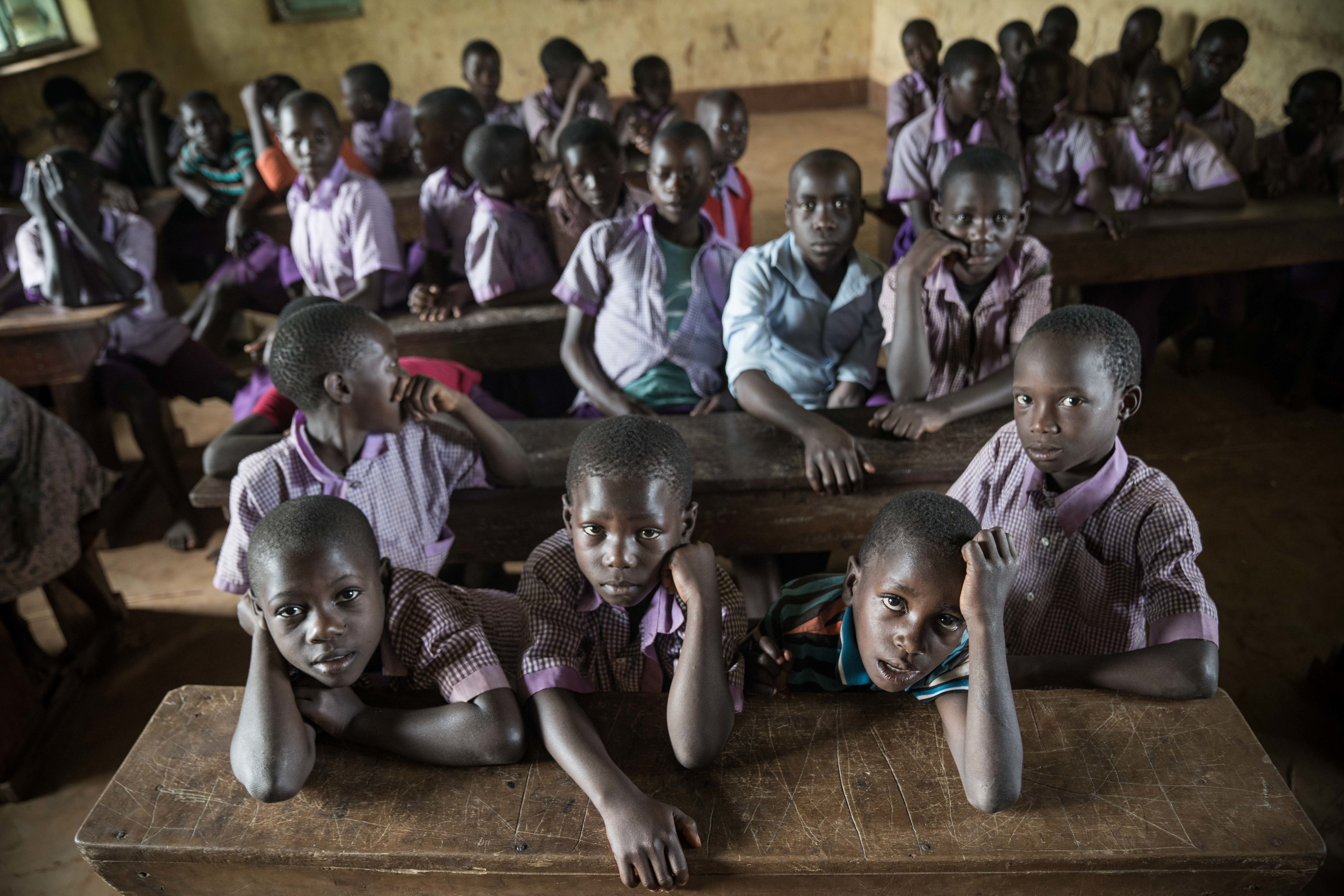 Alunos de Uganda estão sentados em bancos dentro de uma classe.