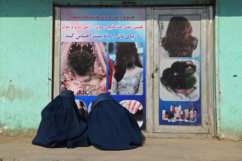 Afghan burqa-clad women sit in front of a beauty salon.