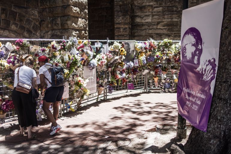 A couple stand by a wall of flowers set up in remembrance of the late Archbishop Desmond Tutu