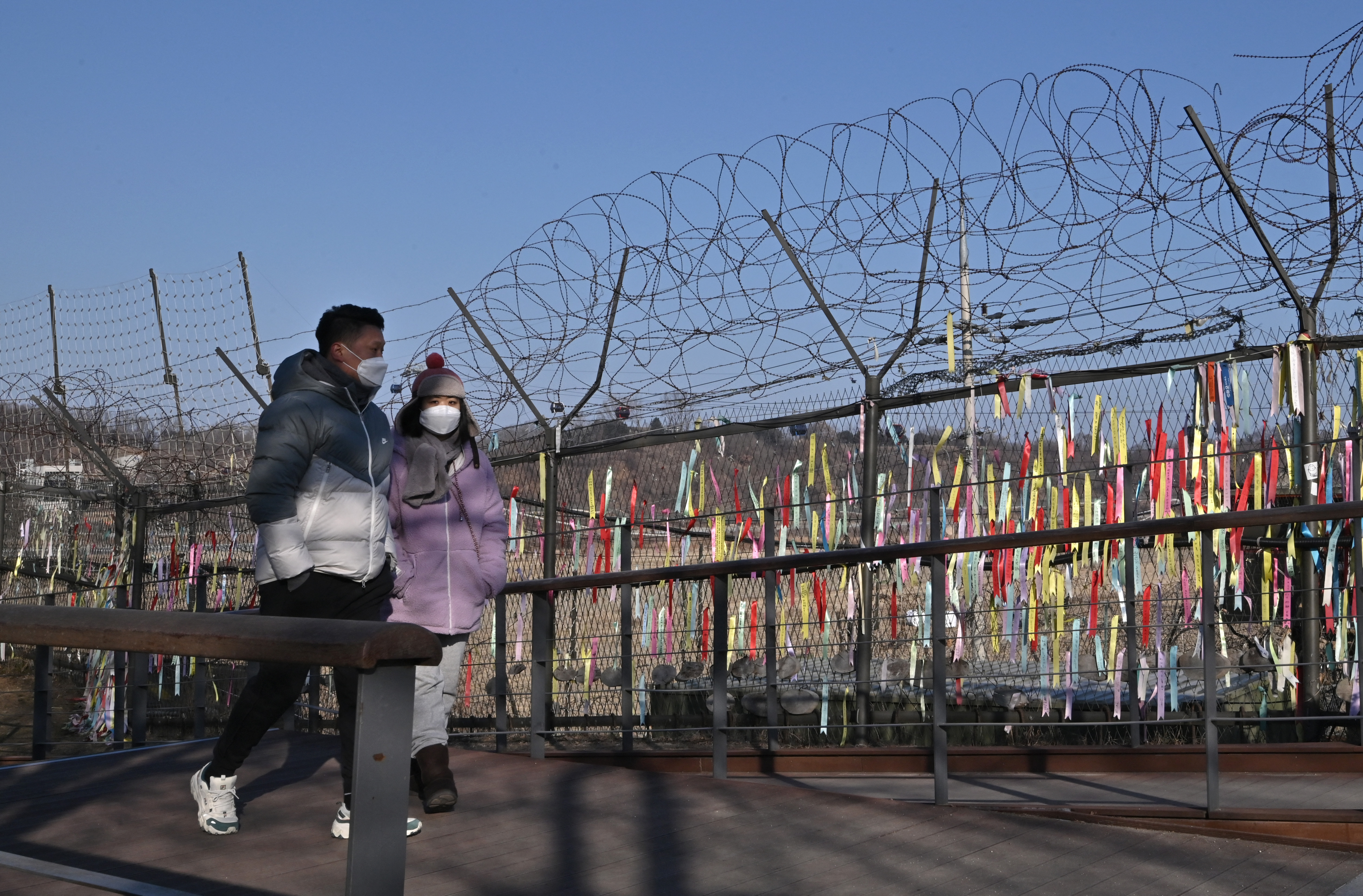 I visitatori passano davanti a una recinzione militare decorata con nastri che desiderano la pace e la riunificazione della penisola coreana nel parco della pace di Imjingak vicino alla zona demilitarizzata (DMZ) che divide le due Coree a Paju il 1 gennaio 2022